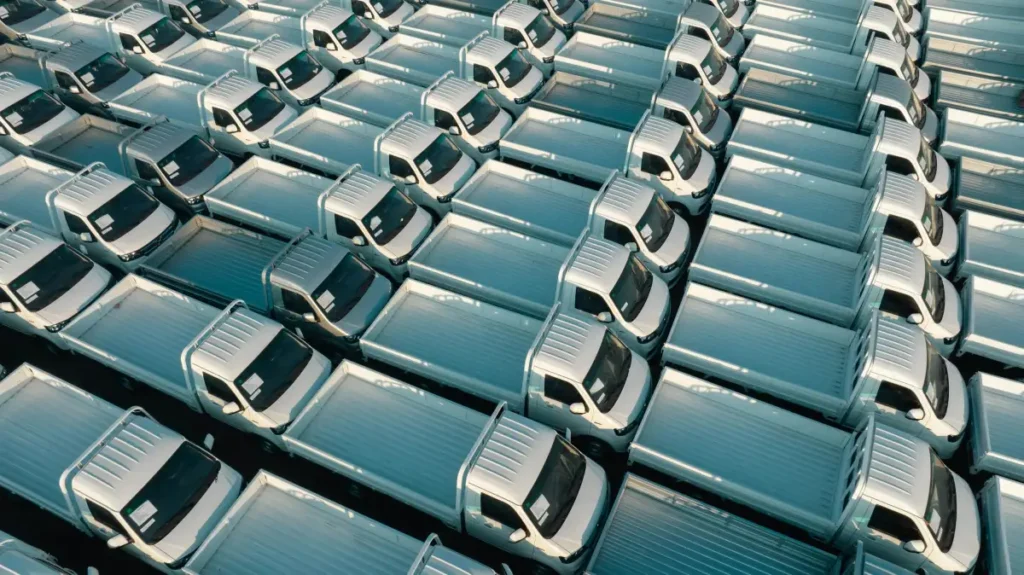 Deretan truk putih terparkir rapi membentuk grid, menggambarkan armada kendaraan operasional perusahaan logistik